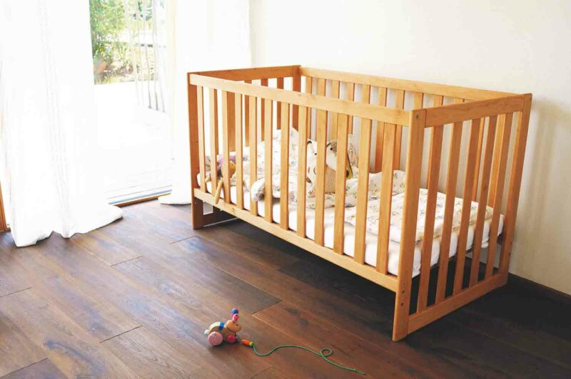 Ein mitwachsendes Kinderbett aus Naturholz für ein Baby steht am Fenster.