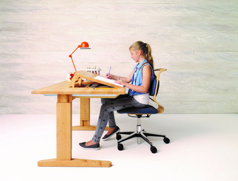 Kind sitzt an einem Schreibtisch aus Massivholz, der höhenverstellbar ist und malt. 